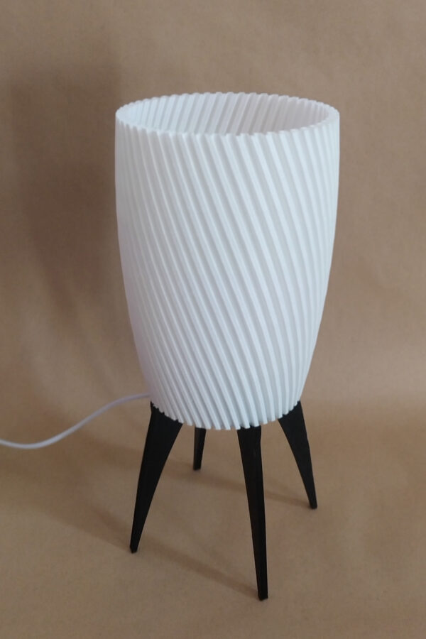 Lampe ZAMBI à pieds fins noirs avec abat-jour blanc strié, conçue avec impression 3D, sur un fond flou.
