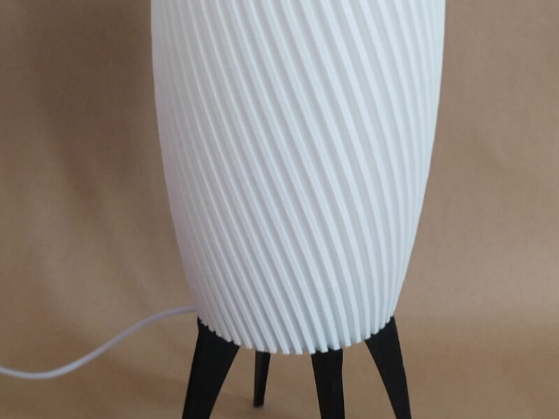 Lampe ZAMBI à pieds fins noirs avec abat-jour blanc strié, conçue avec impression 3D, sur un fond flou.