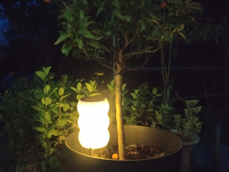Lampe solaire de jardin "GUINGET" imprimée en 3D en plastique recyclable, éclairant un pot de plante la nuit.