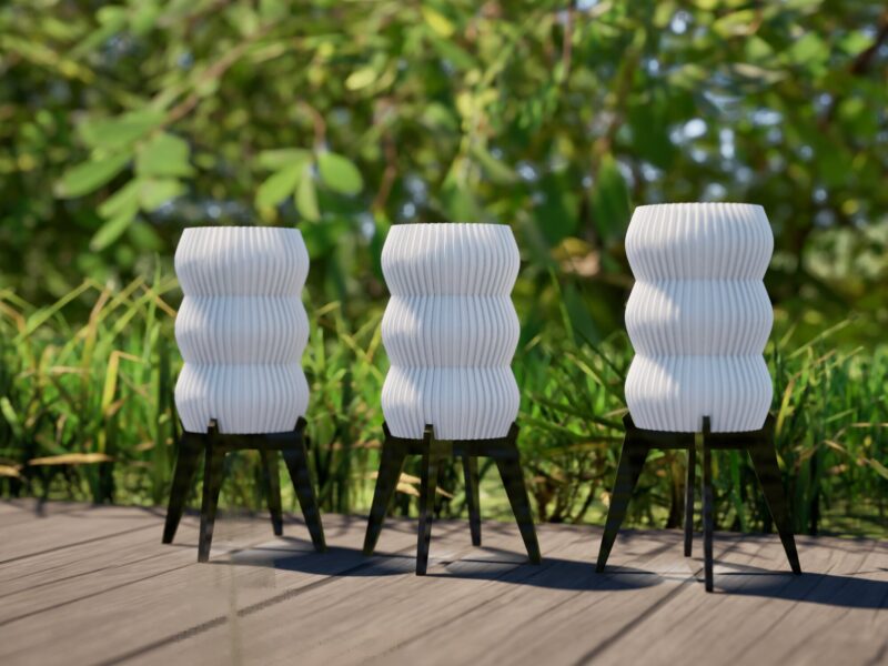 Trois lampes solaires de jardin "GUINGET" imprimées en 3D en plastique recyclable, disposées sur une terrasse en bois à côté d'un espace vert.