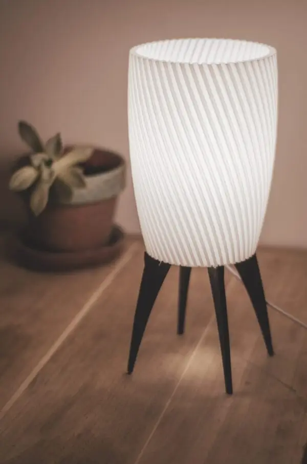 Lampe ZAMBI allumée sur un sol en bois avec une plante en arrière-plan