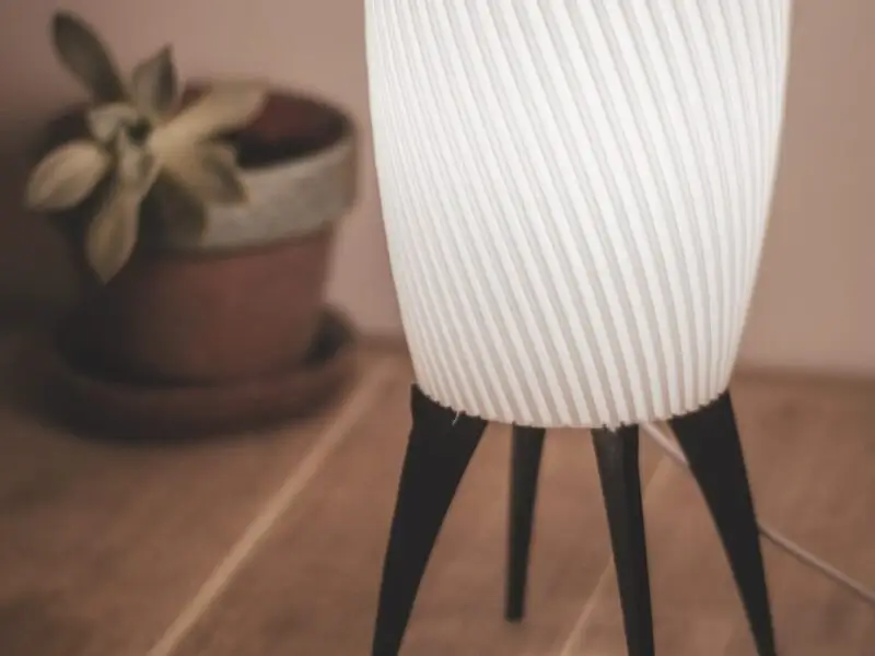 Lampe ZAMBI allumée sur un sol en bois avec une plante en arrière-plan