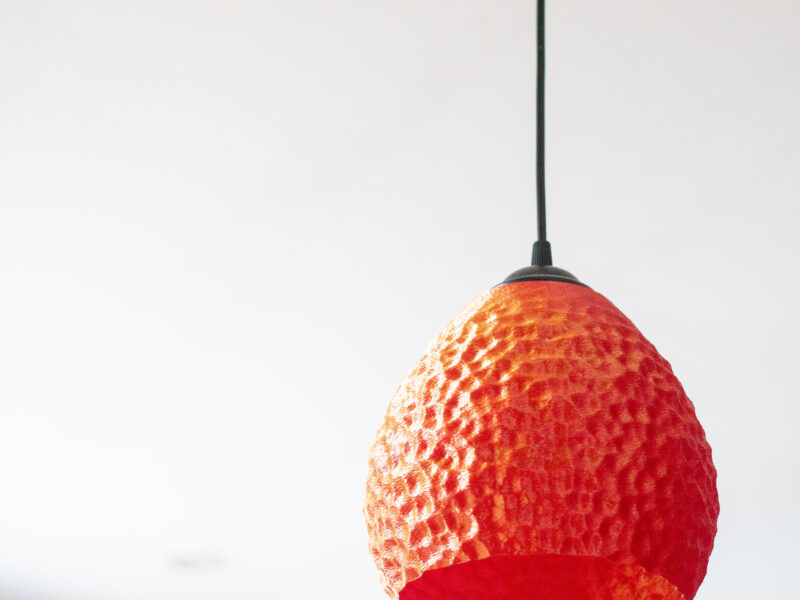 Lampe suspendue rouge imprimée en 3D avec un motif texturé, suspendue dans une pièce lumineuse.