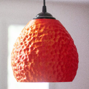 Lampe suspendue rouge texturée, imprimée en 3D, dans une pièce lumineuse.