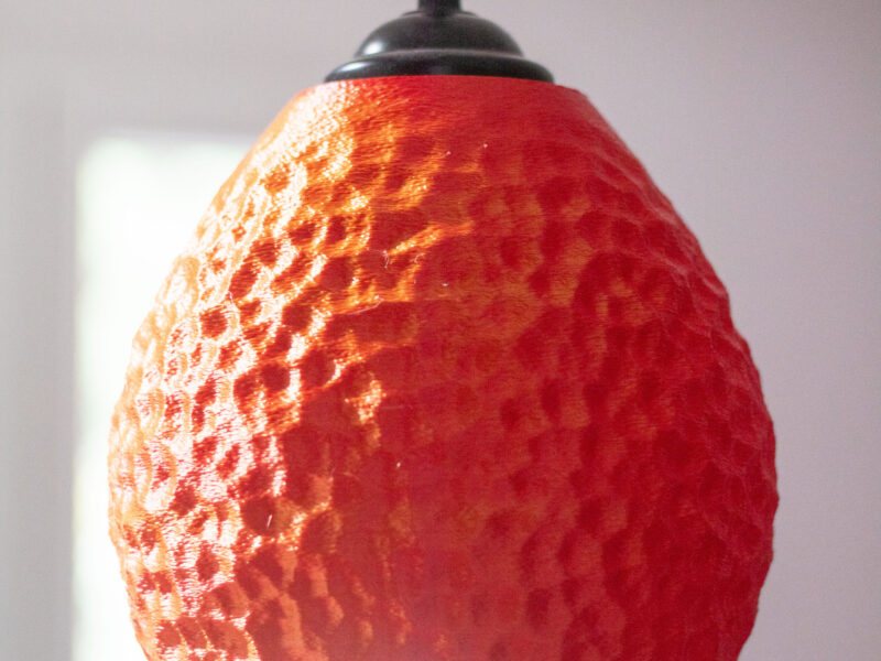 Lampe suspendue rouge texturée, imprimée en 3D, dans une pièce lumineuse.