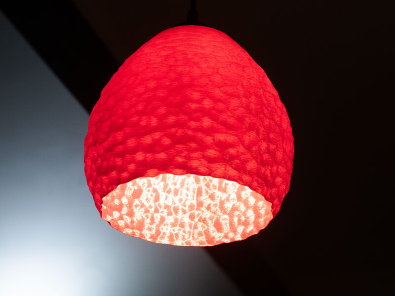 Lampe suspendue rouge imprimée en 3D avec un motif sculpté et un éclairage doux.