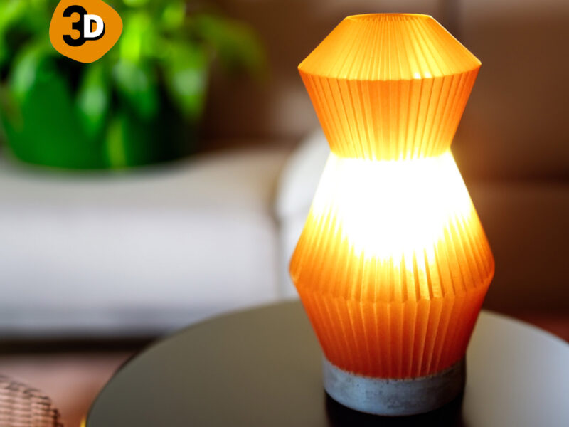 Lampe Voyager orange imprimée en 3D avec un design plissé, éclairant une table noire dans un salon moderne.