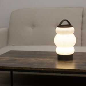 Lampe BUDO allumée sur une table en bois, diffusant une lumière douce dans un salon épuré.