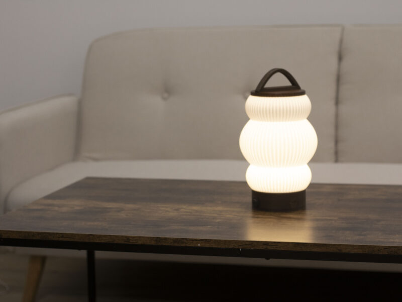 Lampe BUDO allumée sur une table en bois, diffusant une lumière douce dans un salon épuré.