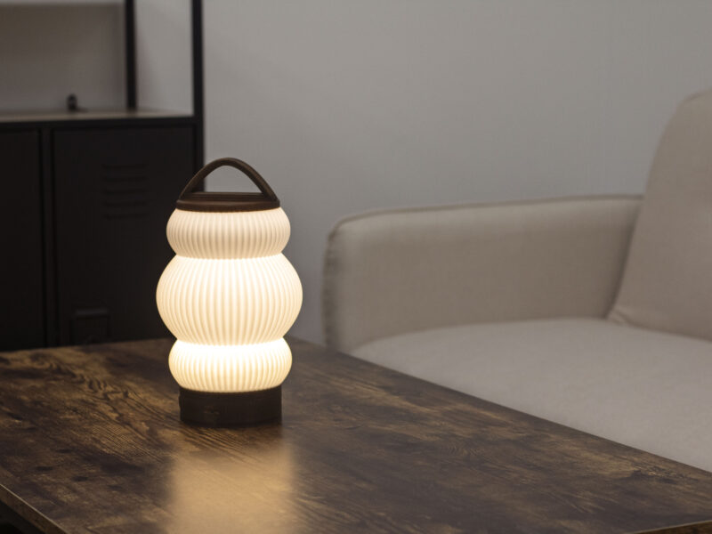 Lampe BUDO allumée sur une table en bois, créant une ambiance cosy dans un salon moderne.