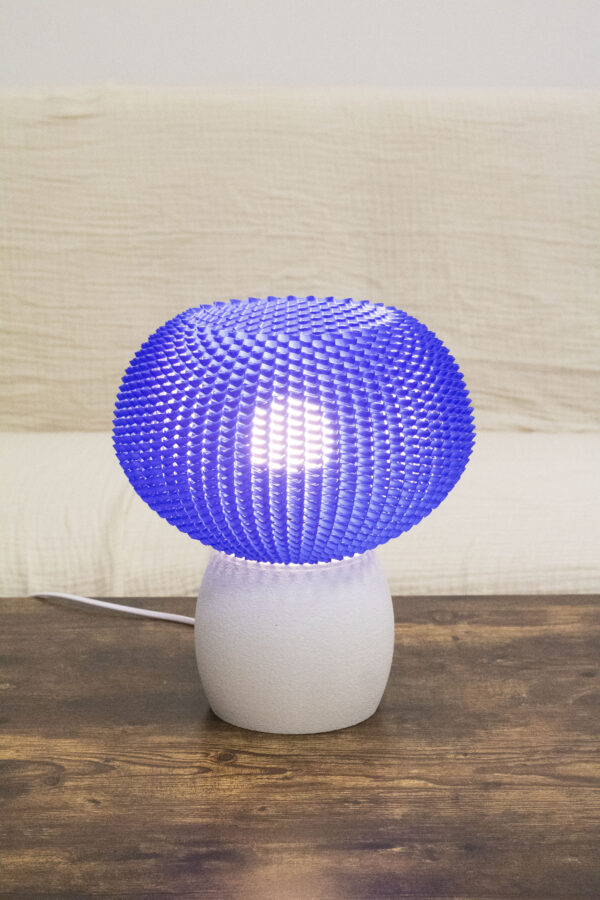 Lampe de table au design moderne avec un abat-jour bleu texturé et une base blanche mate, posée sur une table en bois.