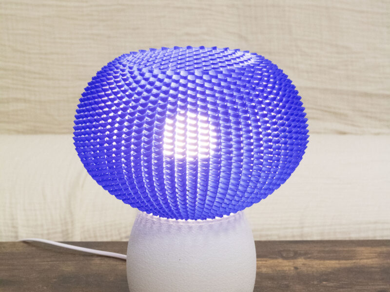 Lampe de table au design moderne avec un abat-jour bleu texturé et une base blanche mate, posée sur une table en bois.