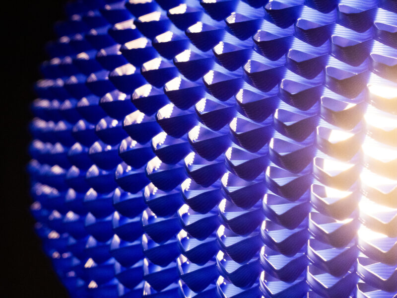 Gros plan sur un abat-jour bleu texturé laissant passer une lumière chaude et tamisée. Titre : Texture lumineuse d’un abat-jour design