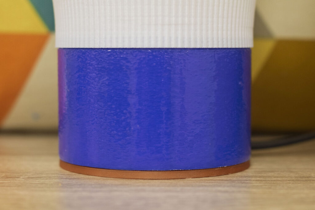 Gros plan sur la base bleue brillante et cylindrique d’une lampe COCO avec un socle contrastant jaune curry.