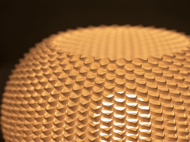 Gros plan sur l’abat-jour ajouré blanc de la lampe BULO, imprimé en 3D et diffusant une lumière douce.